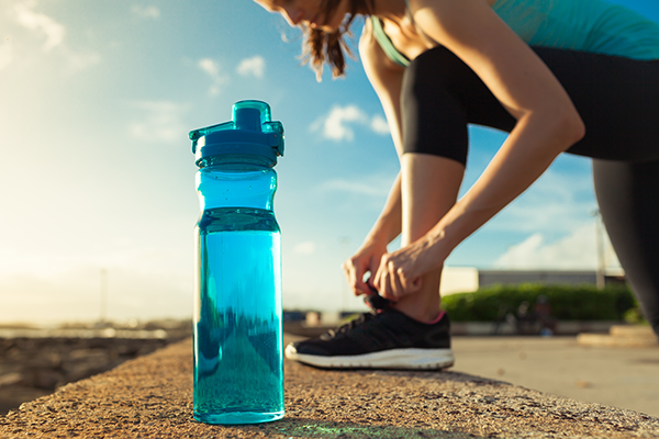 water in blue bottle next to runner lacing up shoes