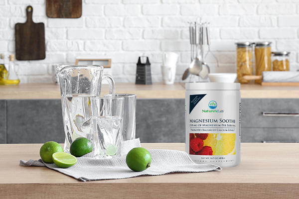 Glass pitcher of water next to limes and Magnesium Soothe supplement in a kitchen