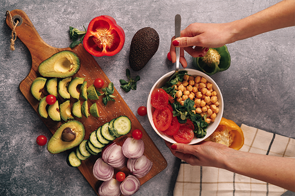 Wood platter and serving bowl of fruit and vegetables on gray stone background