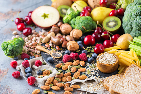 Assorted fibrous foods on surface. Grain bread, pasta, almonds, berries, broccoli, chia and more