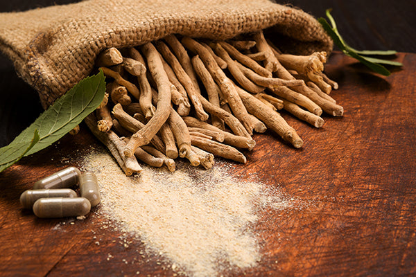 ashwagandha root in powder form and capsules on wooden table
