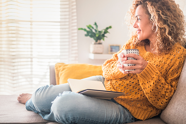 smiling woman enjoying hot beverage and reading a book