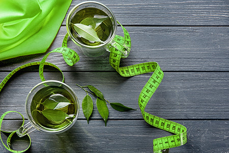 Green tea leaves on table with measuring tape; weight loss concept