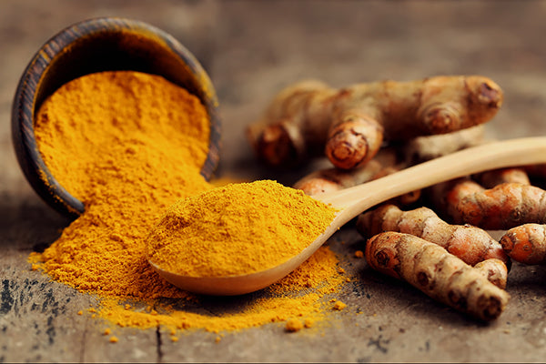 Wooden bowl of turmeric powder next to turmeric root