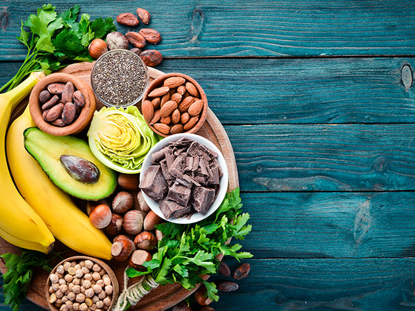 Foods containing magnesium (chocolate, nuts, avocado, bananas) on a blue wood background