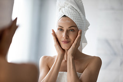 Woman applying face cream in front of mirror