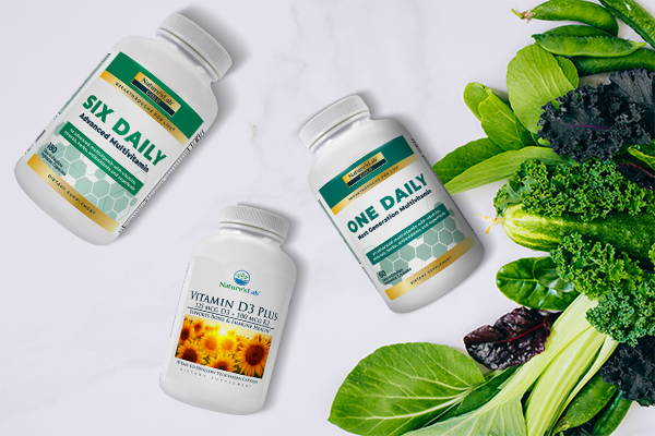 Multivitamin One Daily, Six Daily and Vitamin D3 Plus K2 next to leafy green vegetables