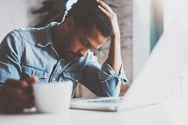 Man looks tired while working on his laptop and drinking coffee.