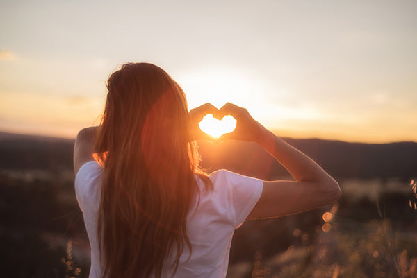 Woman standing in sunshine with back to camera, making heart shape with hands
